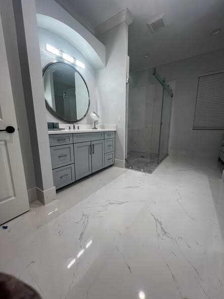Grey shaker bathroom vanity set into an arched alcove, with a round mirror and a glazed walk-in shower alongside